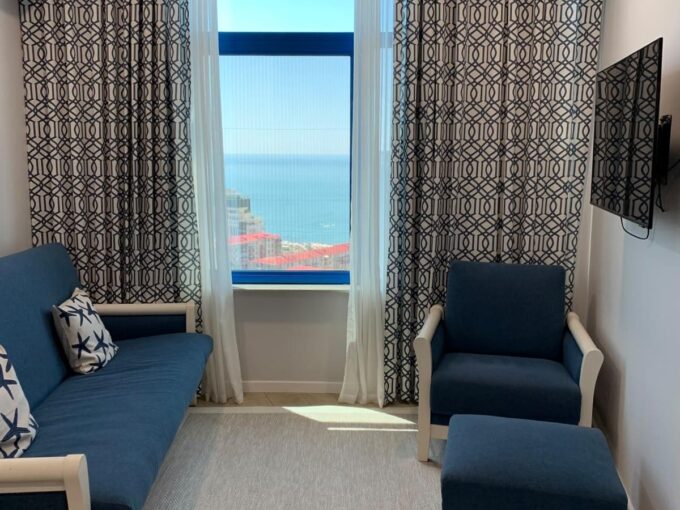 Зона гостиной с диваном, креслом у окна и телевизором в апартаментах ЖК Yalcin Star Residence в Батуми