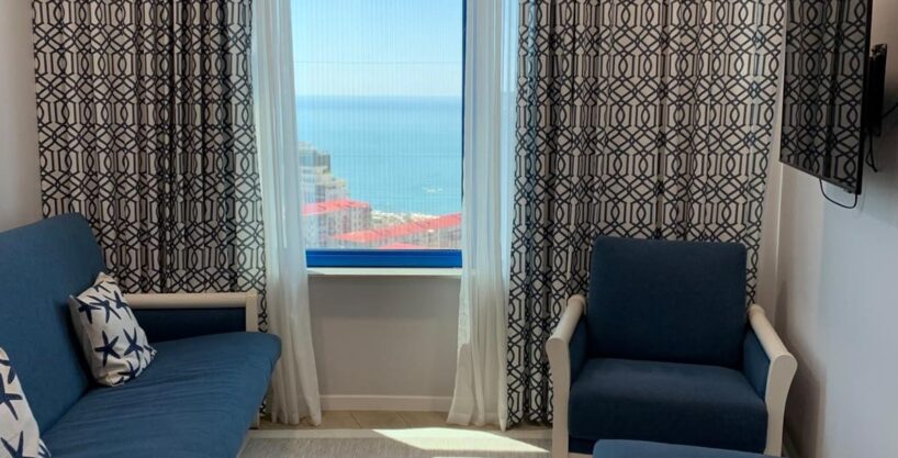 Зона гостиной с диваном, креслом у окна и телевизором в апартаментах ЖК Yalcin Star Residence в Батуми